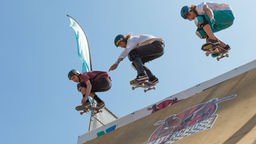 Drei Skateboarder springen gleichzeitig in steile Halfpipe.