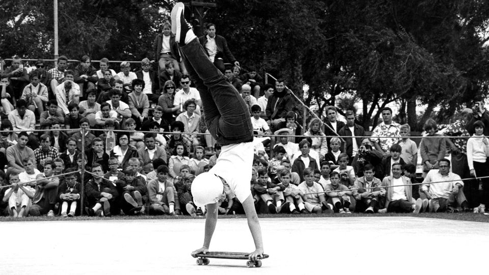 Scharz-weiß Foto aus den 1960er Jahren: Skateboarderin Lauri Turner macht während eines Wettbewerbs Handstand auf einem Skateboard.