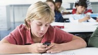 Junge spielt in einem Klassenzimmer mit seinem Handy.