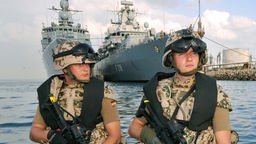 Zwei deutsche Marine-Soldaten sitzen in einem Schnellboot. Im Hintergrund: Fregatte 'Karlsruhe' .