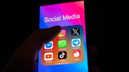 Finger über einem Handybildschirm, auf dem Icons verschiedener Social-Media-Apps eingeblendet sind.