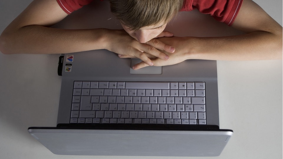 Junge liegt mit Laptop auf dem Bett.