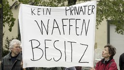 Demonstranten halten ein Plakat mit der Aufschrift "KEIN PRIVATER WAFFENBESITZ" hoch.