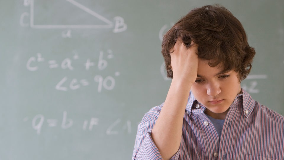 Junge vor einer Tafel mit Matheaufgaben.