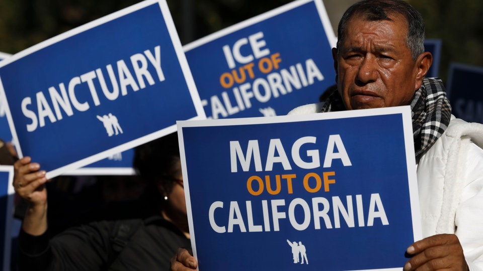 Demonstrant hält blaues Schild mit Aufschrift "MAGA out of California".