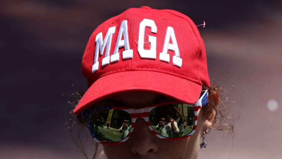 Eine Frau mit Sonnenbrille trägt rote Baseball-Kappe mit der Aufschrift MAGA.