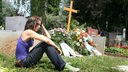 Eine junge Frau sitzt trauernd neben einem frischen Grab auf dem Friedhof.