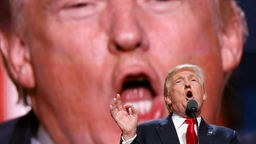 Donald Trump bei Rede, im Hintergrund wird sein Gesicht auf einer Leinwand groß gezeigt.