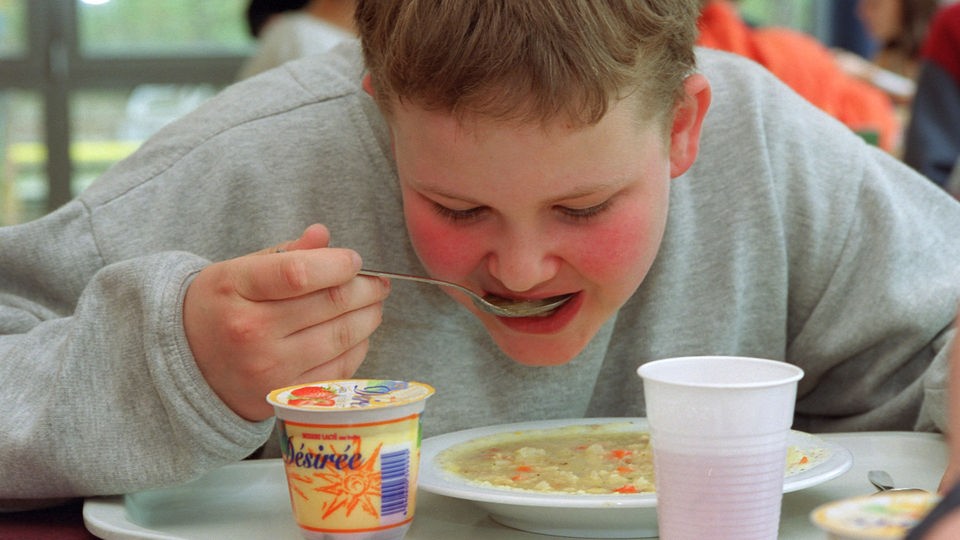Übergewichtiger Junge löffelt Suppe.