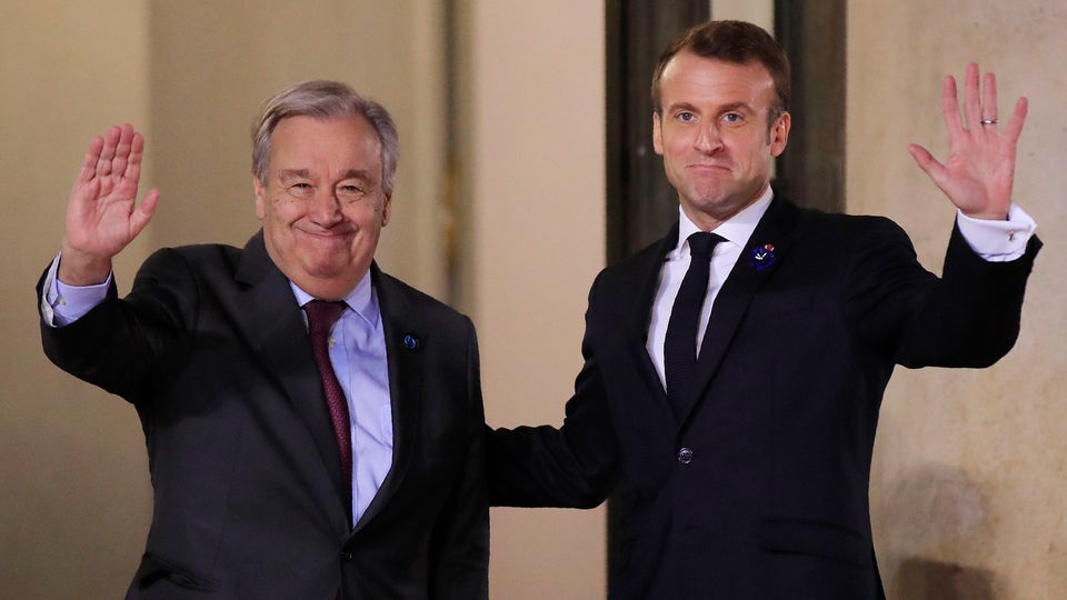 António Guterres und Frankreichs Präsendent Macron stehen nebeneinander und winken in Kamera.