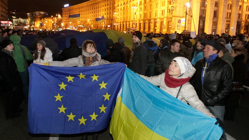 Demonstrantinnen halten die Fahnen der Ukraine und der Europäischen Union nebeneinander.