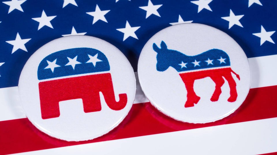 Das Logo der Republikanischen Partei und das Logo der Demokratischen Partei auf einer us-amerikanischen Flagge.