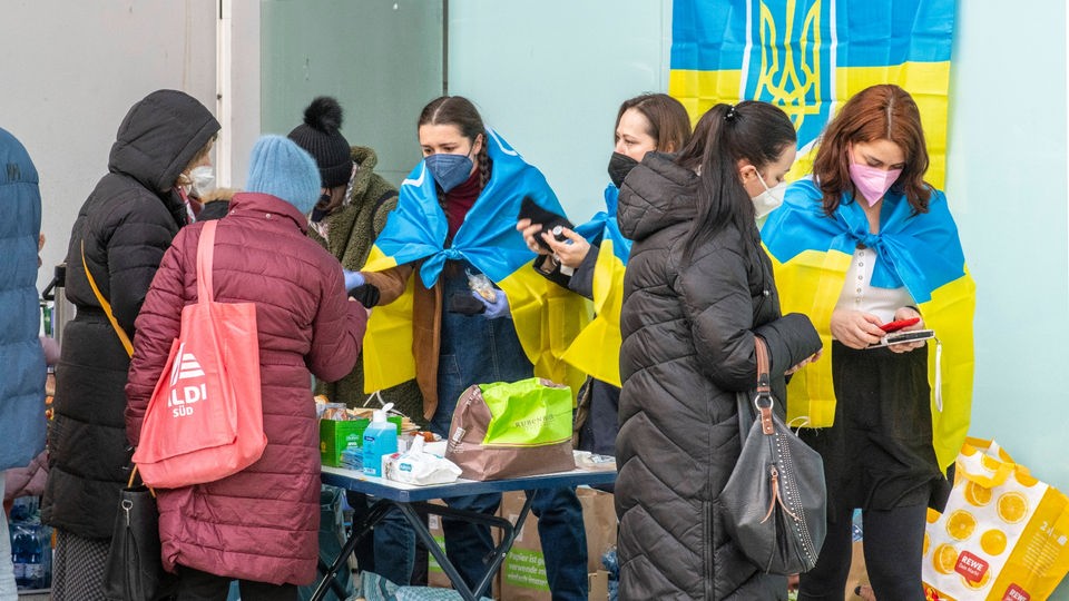 Frauen mit umgehängten Ukraine-Fahnen sprechen mit Geflüchteten.