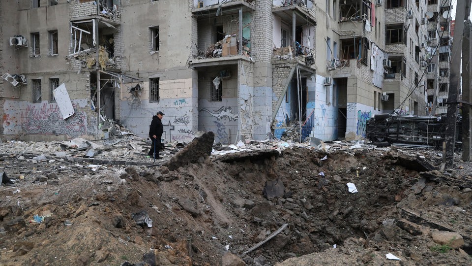 Ein Anwohner steht am Bombenkrater vor einem beschädigten Wohnhaus.