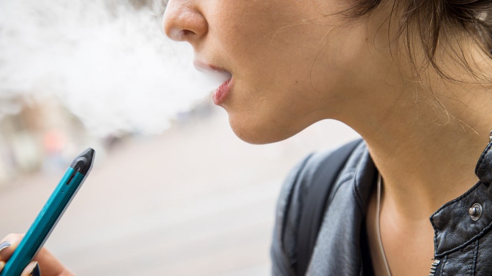 Frau hält E-Zigarette, Rauch kommt aus ihrem Mund.