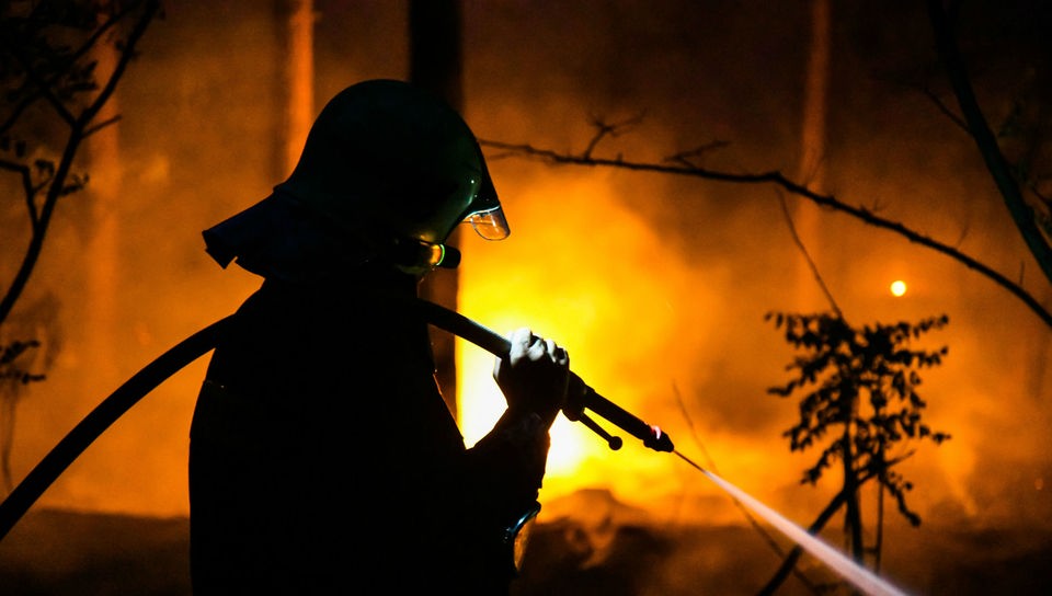 Feuerwehrmann bekämpft in Dunkelheit mit einem Wasserschlauch einen Waldbrand.