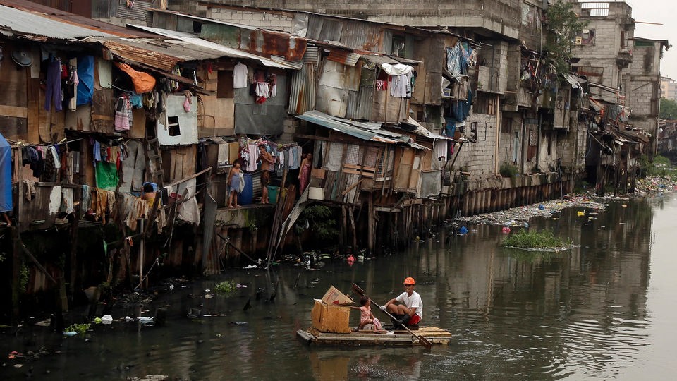 Ein Mann steuert sein Floß durch einen Fluss zwischen den Hütten der Slums in Manila.