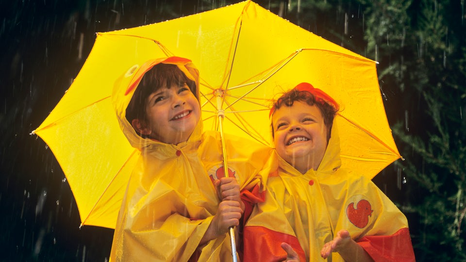 Zwei Kinder in gelber Regenkleidung freuen sich. 