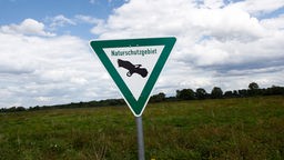 Ein Schild mit der Aufschrift Naturschutzgebiet steht auf einer weiten Wiesenlandschaft.