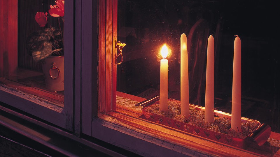 Vier Adventskerzen stehen im Fenster, nur eine von ihnen brennt.