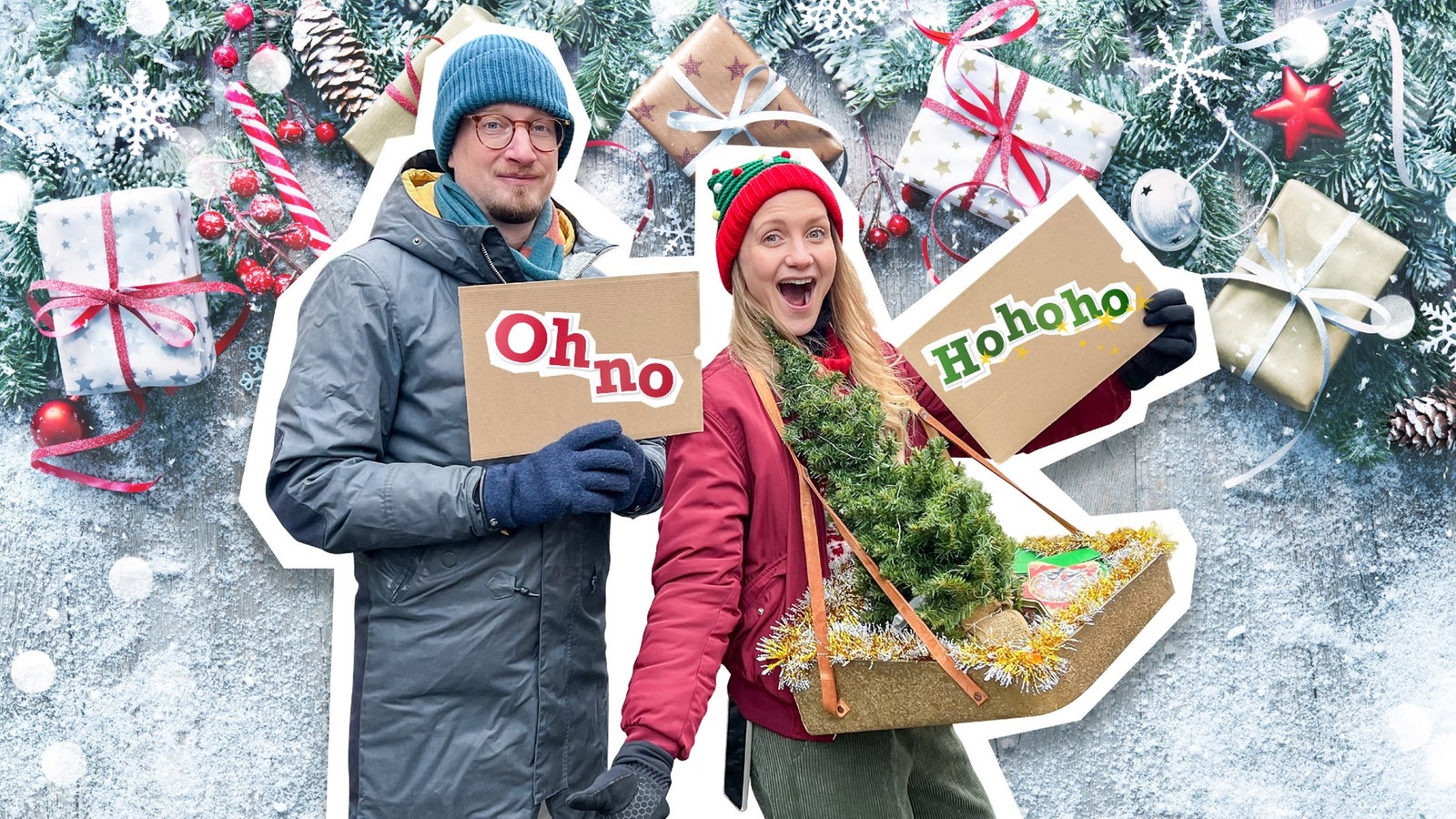 Jana trägt ein Weihnachtsoutfit und strahlt. Robert steht neben ihr und schaut skeptisch. Die beiden halten Pappschilder in der Hand. Auf Roberts Schild steht „Oh No“. Auf Janas Schild steht „Hohoho“.