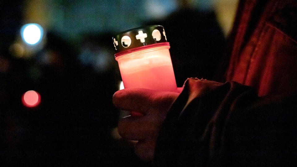 Hand hält rote Friedhofskerze in Dunkelheit.