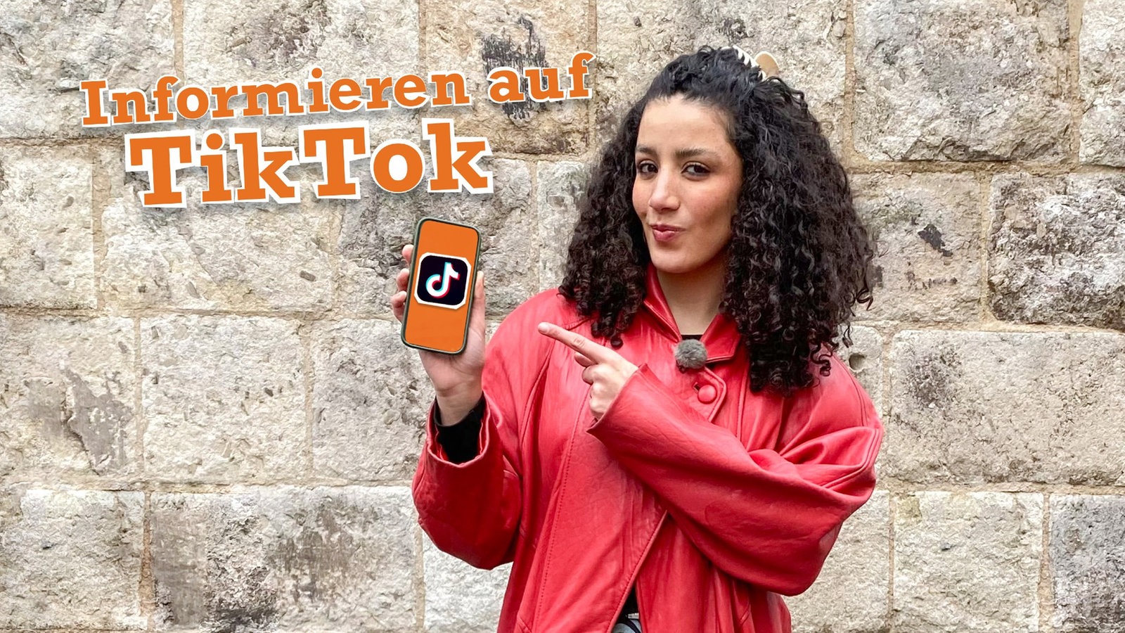 Reporterin Tessniem steht vor Mauer und hält ein Smartphone in der Hand, darauf TikTok-Logo.