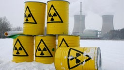 Gelbe Tonnen mit Strahlungszeichen stehen vor Atomkraftwerk.