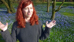 Malin steht mit erhobenen Händen vor einer Blumenwiese.
