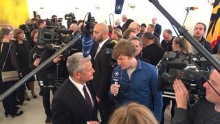 Robert interviewt Bundespräsident Joachim Gauck, die beiden stehen zwischen vielen Kameraleuten und Mikrofonen.