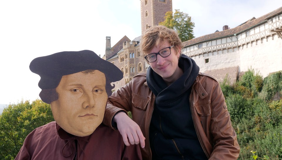 Robert neben einer übergroßen Pappmaske Martin Luthers.