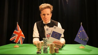 Johannes als Croupier verkleidet am Pokertisch, mit britischer und europäischer Spielkarte.
