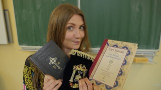 Reporterin Jana mit einer Bibel, einer Tora und einer deutschen Übersetzung des Koran.