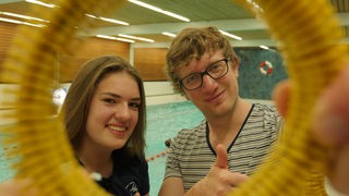Robert und Schülerin Antonia schauen in Schwimmbad durch einen Tauchring.