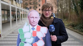 Robert steht neben einem Pappaufsteller von Präsident Putin, der mit 'Daumen hoch' und 'Daumen-runter'-Zetteln beklebt ist.