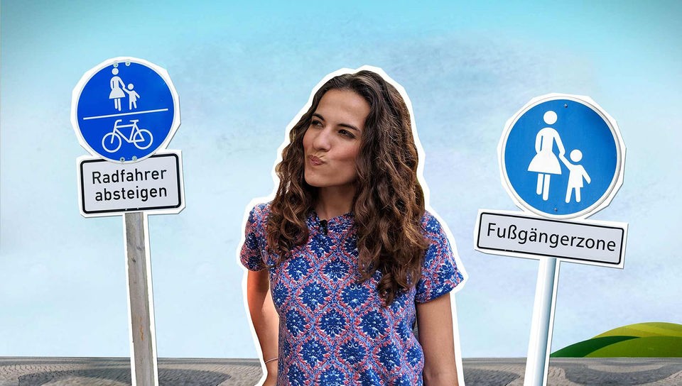Mona steht grübelnd vor einem blauen Hintergrund. Links und rechts neben ihr stehen zwei Verkehrsschilder mit den Aufschriften „Radfahrer absteigen“ und „Fußgängerzone“. 