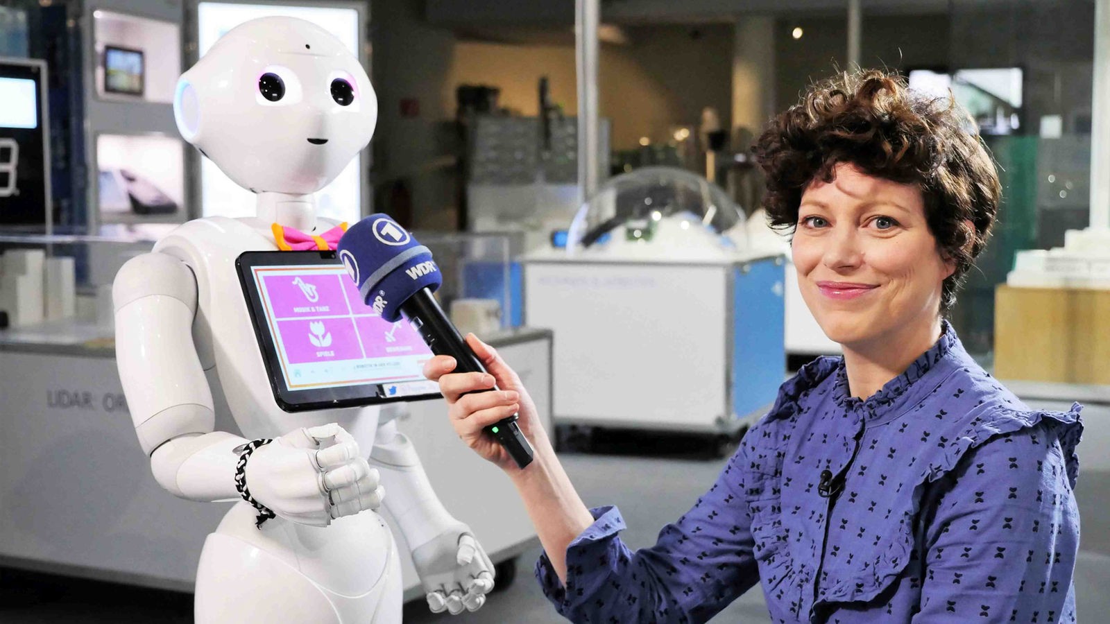 Malin hält dem humanoiden Roboter 'Pepper' ihr Mikro hin.