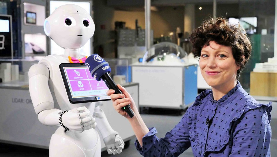Malin hält dem humanoiden Roboter 'Pepper' ihr Mikro hin.