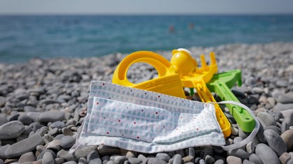 Sandspielzeuge und Mund-Nasen-Schutz liegen auf Strand.