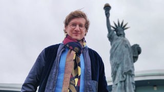 Reporter Robert steht vor einer nachgebauten Freiheitsstatue, die vor einem US-Diner in Deutschland steht.