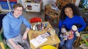 Robert sitzt mit Anne Chebu an einem Kindertisch, auf dem vielfältige und diverse Spielsachen liegen. Es gibt eine Schwarze und eine asiatische Puppe und Buntstifte in unterschiedlichen Hauttönen.