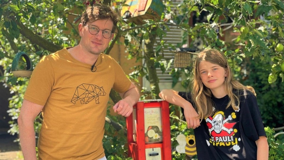 Reporter Robert und Jonte (14) stehen vor seinem umgebauten Kaugummiautomaten. Daraus kann man sich nun Samen für Blühwiesen ziehen.