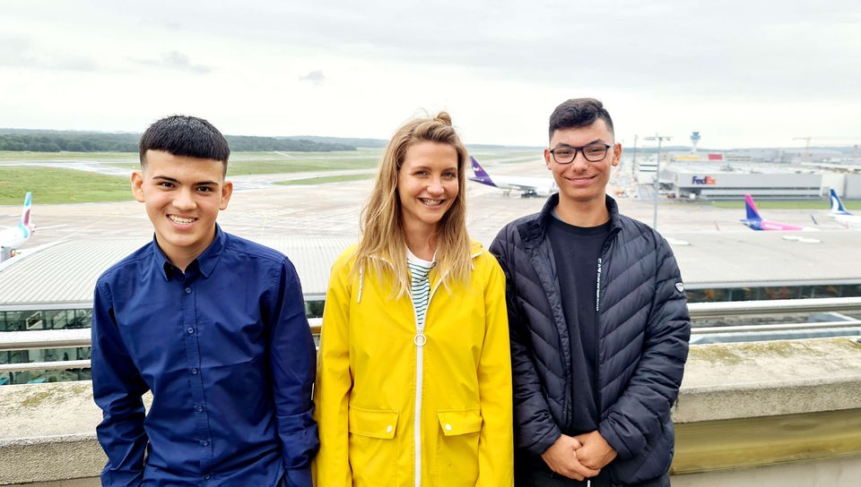 Mahdi, Jana und Karim stehen auf der Besucherterrasse des Flughafen Köln/Bonn. Im Hintergrund sieht man das Rollfeld und einige Flugzeuge.