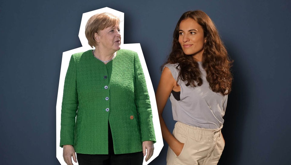 Mona steht neben einem Foto von Angela Merkel und schaut sie an.