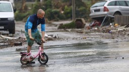Mann schiebt rosafarbenes Kinderrad über eine Straße im Überschwemmungsgebiet.