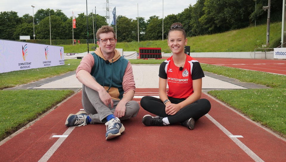 Robert und Friederike sitzen auf der Weitsprung-Bahn bei einem Para-Leichtathletik-Wettbewerb in Leverkusen.