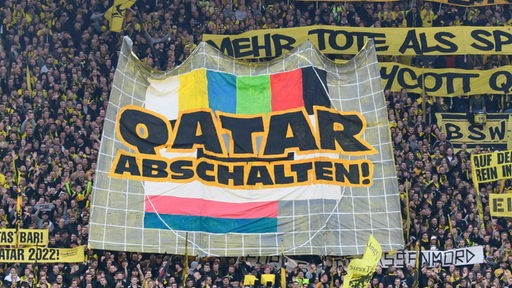 Fans von Borussia Dortmund halten auf der Stadiontribüne ein Transparent mit der Aufschrift 'Qatar abschalten'.