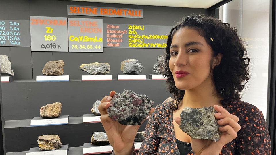 Tessniem hält zwei Gesteine in der Hand, die seltene Erden enthalten.