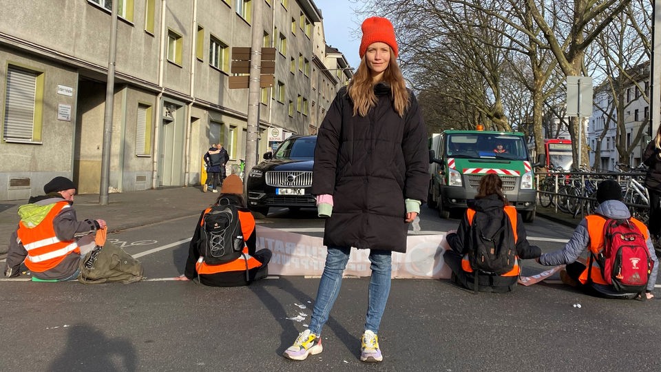 Reporterin Jana steht vor einer Straßenblockade der Letzten Generation.