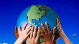 Kinderhände mit unterschiedlichen Hautfarben halten einen Globus.